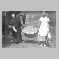 112-0007 Oma Lange und Martha Augustin tragen eine Wanne mit Kuchen. Oma Lange hat fuer alle Feierlichkeiten im Dorf den Kuchen gebacken.jpg